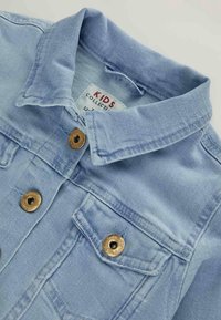 Hellblaue Denimjacke für Kinder mit Kragen, bronzenen Knöpfen und einer vorderen Klappentasche auf weißem Hintergrund.