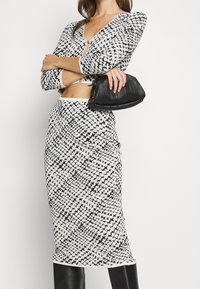 Svartvit mönstrad crop top med långa ärmar och V-ringning, i kombination med en matchande hög midjeskjorta och en texturerad svart handväska.