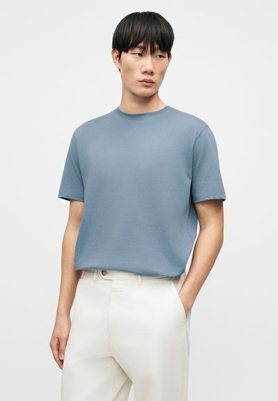 T-shirt bleu à manches courtes en tissu doux, avec un col rond, associé à un pantalon ample de couleur claire.
