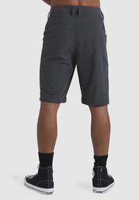Shorts grises con una textura suave, hasta las rodillas, que cuentan con dos bolsillos traseros y trabillas para el cinturón. Combinados con zapatillas negras de caña alta y calcetines.