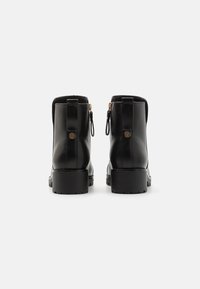 Bottines noires en cuir avec une finition lisse, bout rond et un talon épais. Présentent des accents de fermeture éclair dorés et des tirettes à l'arrière.