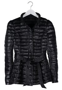 Veste matelassée noire avec manches longues et ceinture nouée à la taille, suspendue sur un cintre blanc sur fond blanc.
