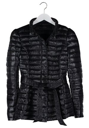 Femme portant une doudoune noire, chemise blanche, jean skinny bleu, bottines noires, tenant un grand sac fourre-tout noir clouté.