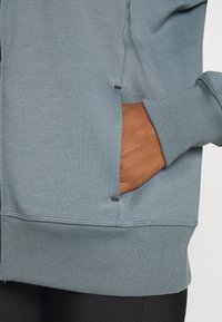 Ljusblå sweatshirt med slim fit, ribbstickade ärmslut och en sidoficka med svarta detaljer. Slät textur och minimala sömnadsdetaljer.