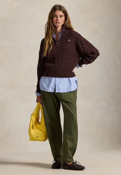 Hnedý sveter s vrkočovým vzorom, svetlomodrá košeľa pod ním, voľné zelené nohavice, žltá kabelka a tmavohnedé mokasíny.