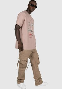 Lyserød bomulds T-shirt med grafisk print, parret med brune cargo bukser med flere lommer og snore, samt hvide sneakers.