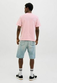 Roze katoenen t-shirt, denim shorts, zwarte sneakers met witte accenten, en gestreepte sokken. Achteraanzicht tegen een effen achtergrond.