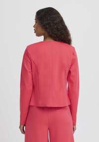 Blazer corail en tissu lisse, doté d'une coupe droite, de manches longues et d'un dos simple avec de légers détails de coutures ajustées.