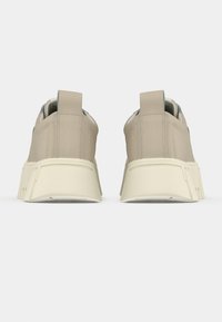 Sneaker beige con materiale liscio, forma rotonda e accenti testurizzati. Presentano una suola spessa color crema e linguette posteriori.