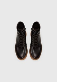 Chaussures montantes en cuir noir avec semelle marron, design à lacets, fermeture éclair sur le côté et accent texturé autour de la semelle.