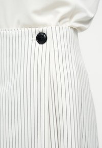 Λευκή φούστα με λεπτές κάθετες μαύρες ρίγες, λεπτομέρεια πλισέ και μαύρο κουμπί στη μέση, σε συνδυασμό με λευκό τοπ καρφωμένο μέσα.