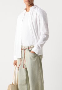 White button-up shirt with a pointed collar, layered over a white t-shirt. Light-colored, loose-fitting trousers with a multicolored drawstring.