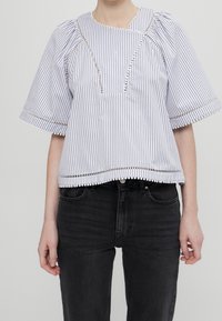 Blouse à manches courtes rayée blanche et bleu marine, avec un décolleté carré, une bordure en dentelle à l'ourlet, et des manches bouffantes à coupe décontractée.