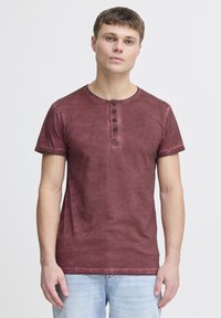 Burgunderfarbenes T-Shirt mit kurzen Ärmeln, rundem Ausschnitt und fünf Knöpfen. Weicher, leicht strukturierter Stoff. Schlichtes Design, lockere Passform.