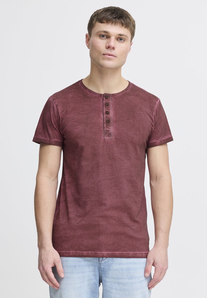 Burgunderfarbenes T-Shirt mit kurzen Ärmeln, rundem Ausschnitt und fünf Knöpfen. Weicher, leicht strukturierter Stoff. Schlichtes Design, lockere Passform.
