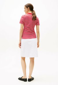 Rood-wit gestreepte shirt met korte mouwen in combinatie met een witte rok tot de knie. Het model draagt zwarte platte schoenen.