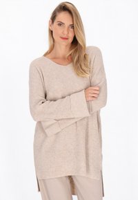 Maglione beige in maglia con vestibilità ampia, scollatura a V e maniche lunghe. Presenta delle fessure laterali all'orlo per una maggiore libertà di movimento.