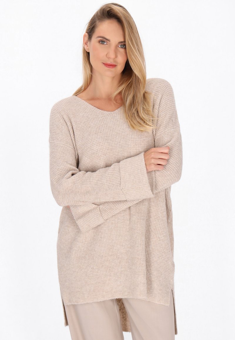 Maglione beige in maglia con vestibilità ampia, scollatura a V e maniche lunghe. Presenta delle fessure laterali all'orlo per una maggiore libertà di movimento.