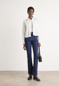 Ruteliste hvit knapp-up skjorte, off-white topp, blå flared jeans, svarte åpne sko, holder en liten svart håndveske.
