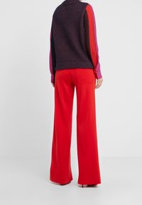 Maglione lavorato a maglia con maniche multicolori nelle tonalità di rosa, rosso e blu navy, abbinato a pantaloni rossi a vita alta e a gamba larga.