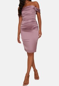 Off-shoulder mauveklänning i slätt tyg med rynkdetaljer längs kroppen, som smalnar av till knälång nederkant. Klara blockklackar.