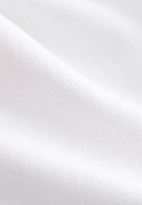 Close-up of soft white fabric with visible fine woven texture and gentle folds creating light and shadow.