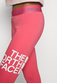 Růžové sportovní legíny s vysokým pasem s bílým logem "THE NORTH FACE", vyrobené z hladkého, elastického materiálu.