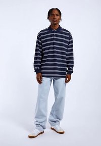 Navy striped long-sleeve polo shirt with white horizontal lines, paired with light blue baggy jeans and white sneakers with gum soles.