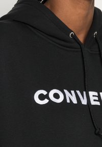 Felpa nera in cotone con cappuccio e cordino, con grande testo ricamato bianco che reca la scritta "CONVERSE" sulla parte anteriore.