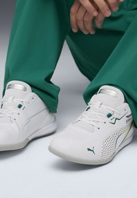 Weiße Sportschuhe mit perforiertem Design und grünen Akzenten. Verfügt über eine strukturierte Sohle und ein glattes Lederoberteil. Minimalistisches Branding-Detail.