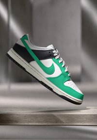 Green, black, and white Nike Dunk sneakers featuring a leather upper, perforated toe, and textured rubber sole. Sole is slightly raised.