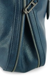 Blauw leren tas met een opvallende zilveren rits en metalen details, met een ronde vorm en zachte randen.