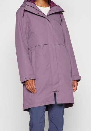 Persoon draagt een lange paarse jas met capuchon, voorzakken en drukknopmanchetten over een blauwe broek.