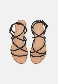 Sandali neri con cinturini, dotati di suola piatta e caratterizzati da più cinturini sovrapposti. La soletta è beige con dettagli cuciti.