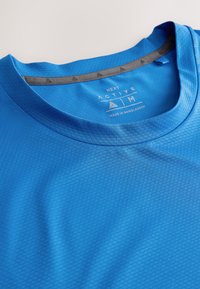 T-shirt de sport texturé bleu avec col rond, taille moyenne, étiqueté "Next Active", fabriqué au Bangladesh.