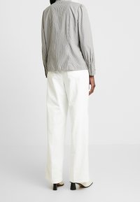 Camicia a righe grigia e bianca, con maniche a sbuffo. Abbinata a pantaloni a gamba larga in corduroy bianchi e stivali con tacco beige.