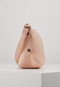 Růžová kožená kabelka s prohnutým tvarem, strukturovaným povrchem a kovovým zapínáním na druk. Popruh je připevněn nahoře.