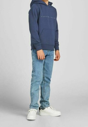 Hoodie marine avec poche kangourou à l'avant et logo ; associé à un jean bleu clair et des baskets blanches avec des accents noirs.