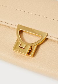 Beige leren portemonnee met textuurafwerking, voorzien van een sluiting in goudkleurig metaal en de merknaam die is ingedrukt op de hardware.