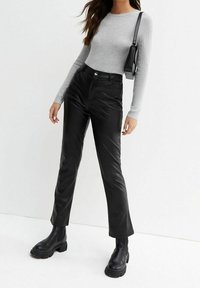 Femme portant un haut gris côtelé à manches longues, un pantalon en cuir noir taille haute, des bottes noires épaisses et un sac à bandoulière noir.