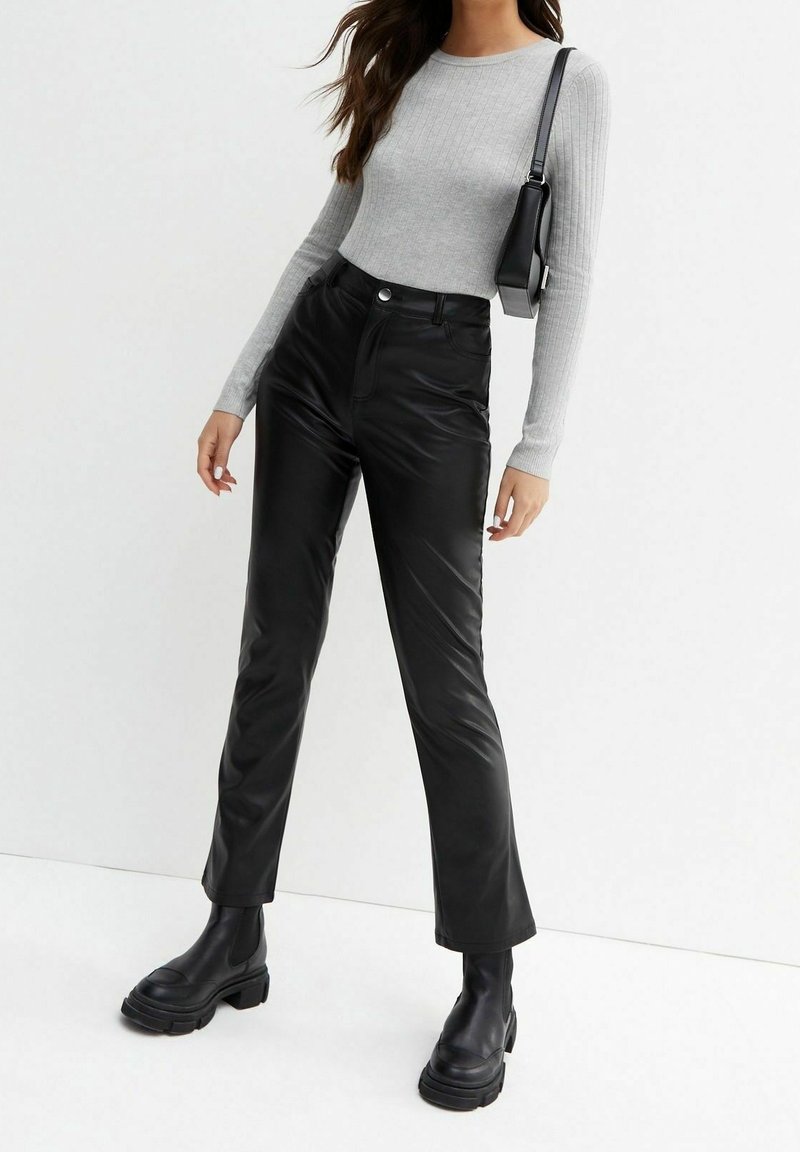 Femme portant un haut gris côtelé à manches longues, un pantalon en cuir noir taille haute, des bottes noires épaisses et un sac à bandoulière noir.