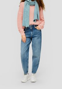 Un pull texturé rose clair associé à un jean en denim bleu taille haute et une écharpe bleu clair. Chaussures : baskets blanches.