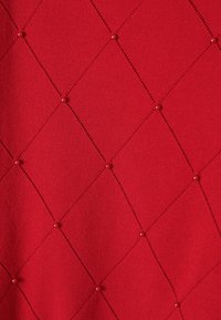 Piros szövet, amelyen gyémánttakaró minta látható, kis kerek díszítésekkel és dekoratív varrással. Simma texture és egységes szín.