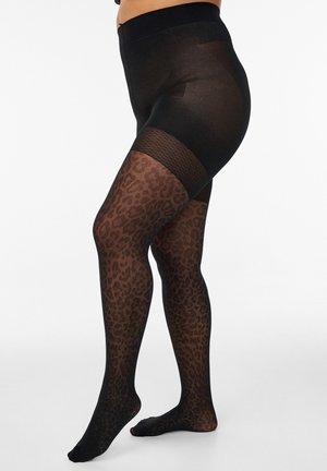 Noge v črnih prosojnih pajkicah z leopardjim vzorcem in trdnim črnim delom hlačk, stoječe na belem ozadju.