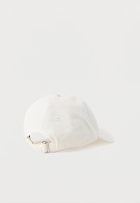 Gorra blanca de algodón con visera curva, diseño de seis paneles y correa metálica ajustable en la parte trasera. Cuenta con ojetes morados para mayor transpirabilidad.