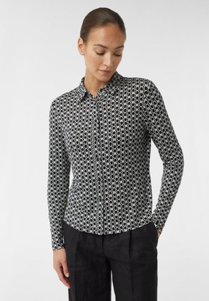 Langärmliges, knöpfbares Hemd in Schwarz und Weiß, mit einem geometrischen Muster aus miteinander verbundenen Formen auf einem glatten Stoff. Mit Kragen-Design.