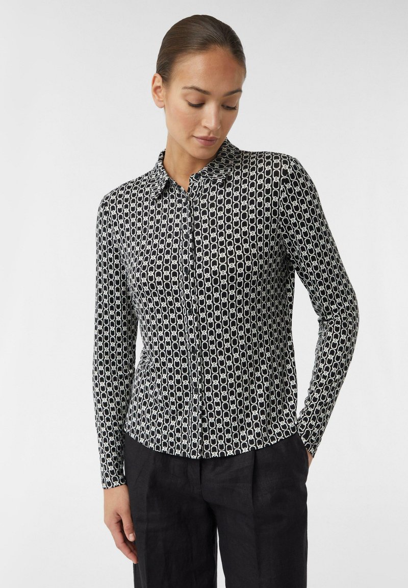 Long-sleeve, button-up shirt in black and white, featuring a geometric pattern of linked shapes on a smooth fabric. Collared design.
