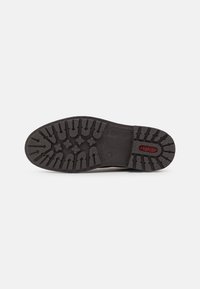 Suola di scarpa in gomma nera con un motivo di battistrada testurizzato e logo "rieker" rosso, progettata per aderenza e durata.