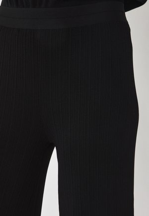 Close-up van zwarte geribbelde gebreide broek die de structuur en elastische tailleband toont op het onderlijf en de bovenbenen van een persoon.