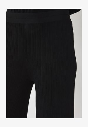 Close-up van zwarte geribbelde gebreide broek die de structuur en elastische tailleband toont op het onderlijf en de bovenbenen van een persoon.